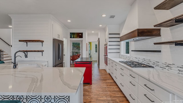 kitchen with light hardwood / wood-style flooring, light stone counters, appliances with stainless steel finishes, and custom range hood