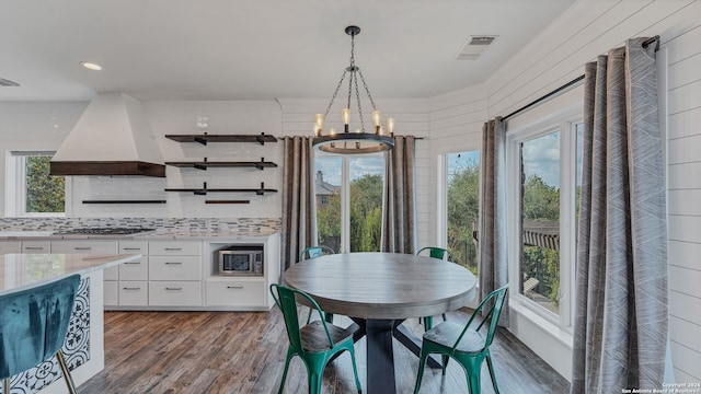 dining space with a notable chandelier, wood walls, and dark wood-type flooring