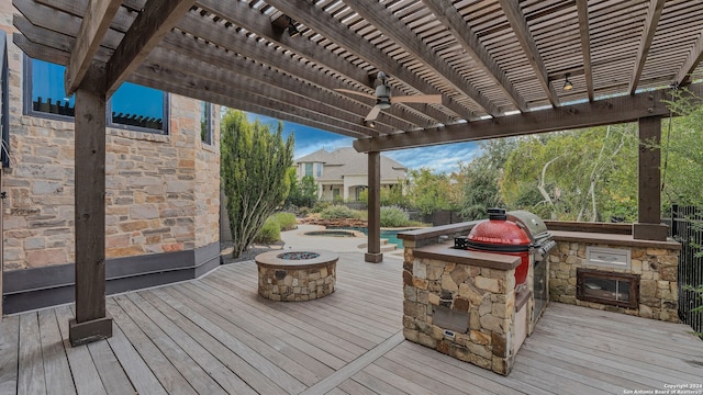 wooden deck featuring a pergola, ceiling fan, an outdoor fire pit, and exterior kitchen