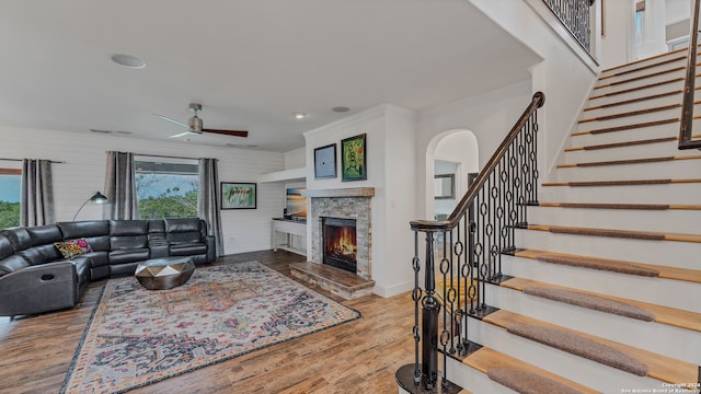 living room with ceiling fan, wood walls, ornamental molding, a fireplace, and light hardwood / wood-style floors