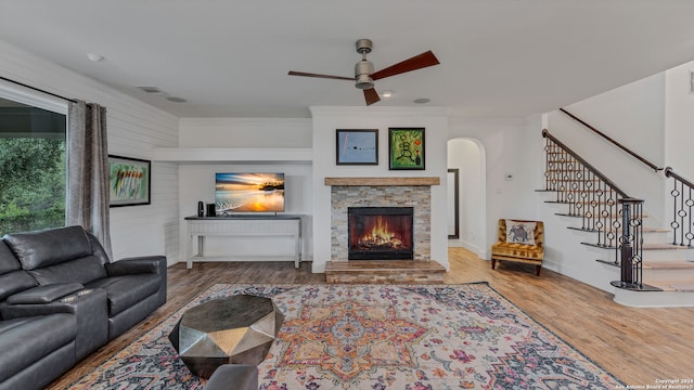 living room featuring wood-type flooring, a fireplace, ornamental molding, and ceiling fan