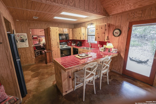 kitchen featuring sink, tile countertops, kitchen peninsula, backsplash, and black appliances