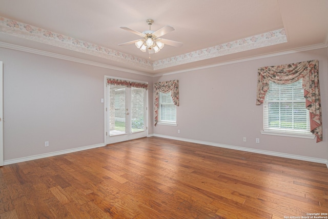 empty room with ceiling fan, a raised ceiling, hardwood / wood-style floors, and a wealth of natural light