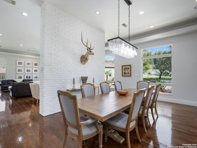 dining space featuring dark wood-type flooring, brick wall, and an inviting chandelier