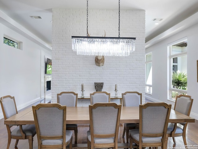 dining room featuring light wood-type flooring, a wealth of natural light, a notable chandelier, and brick wall