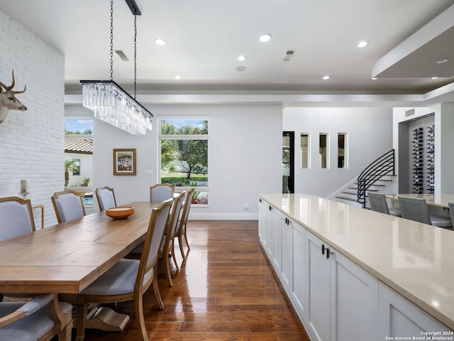 dining room featuring dark wood-type flooring, brick wall, and a notable chandelier