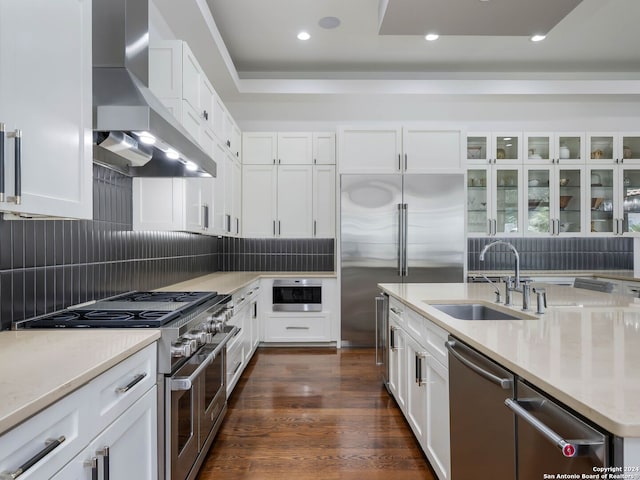 kitchen with wall chimney range hood, sink, high quality appliances, white cabinets, and dark wood-type flooring