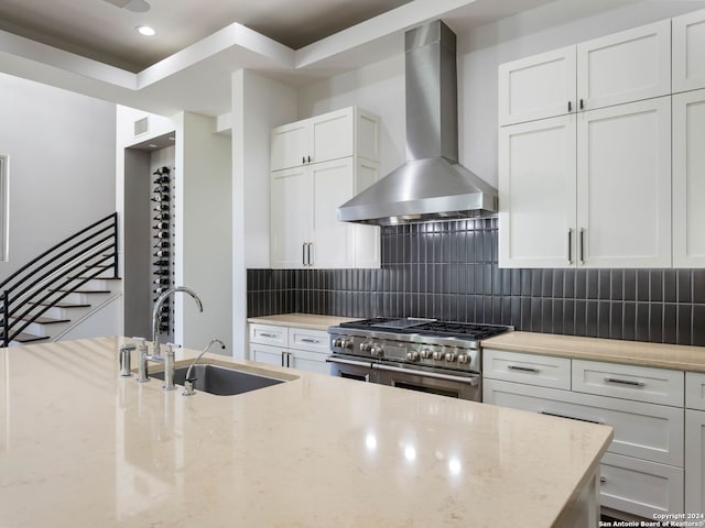 kitchen with wall chimney exhaust hood, sink, light stone counters, and high end stove