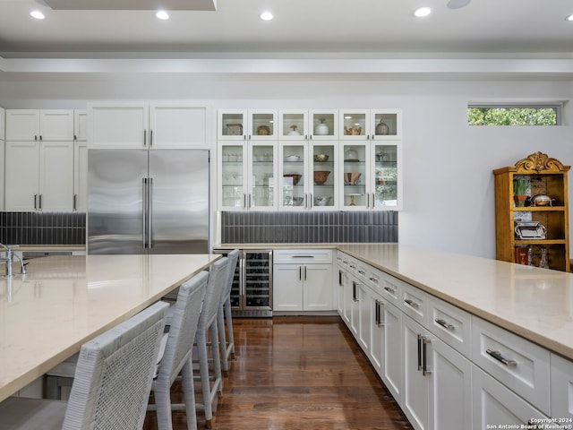 kitchen featuring light stone counters, beverage cooler, built in fridge, white cabinets, and dark hardwood / wood-style flooring