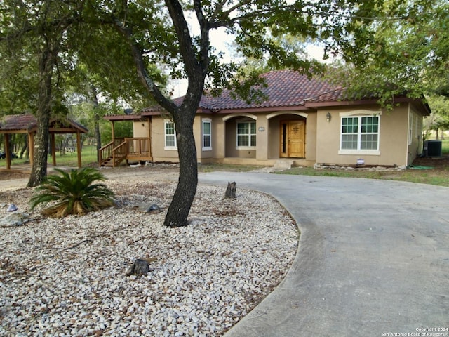 view of front facade featuring central air condition unit, a tile roof, stucco siding, and curved driveway