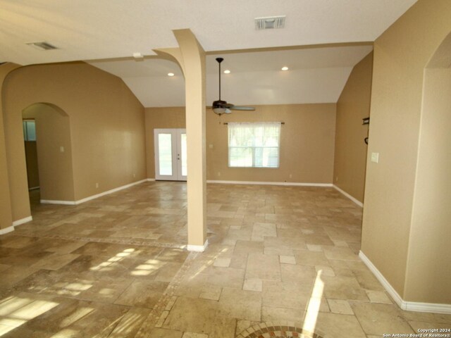 spare room with stone tile floors, vaulted ceiling, arched walkways, ceiling fan, and visible vents