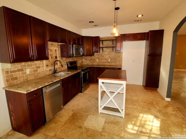 kitchen with sink, decorative backsplash, stainless steel appliances, decorative light fixtures, and light stone countertops