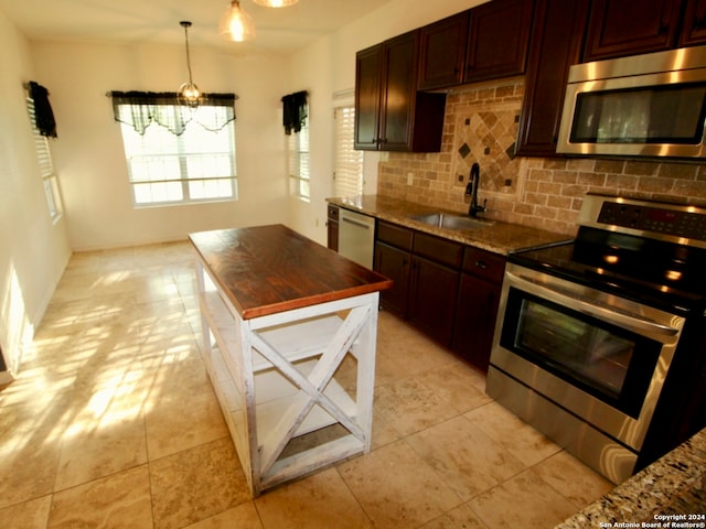 kitchen with tasteful backsplash, butcher block countertops, pendant lighting, stainless steel appliances, and sink