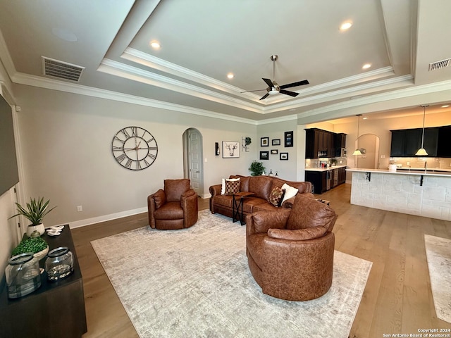 living room with ornamental molding, a tray ceiling, light hardwood / wood-style floors, and ceiling fan