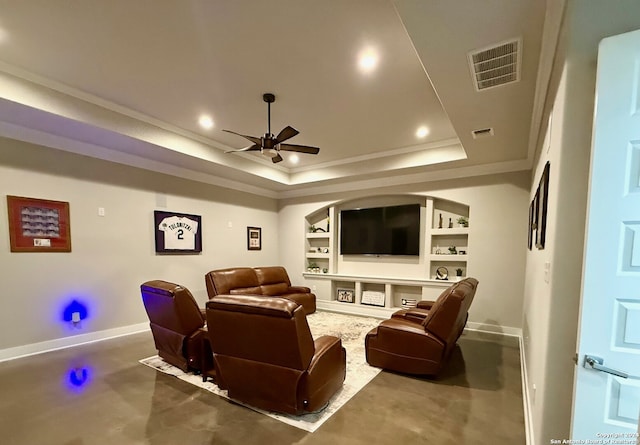 home theater room with a raised ceiling, built in shelves, ornamental molding, and ceiling fan