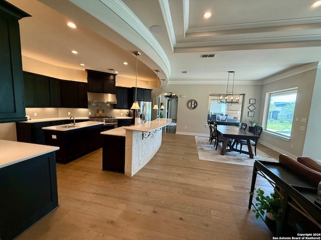 kitchen with appliances with stainless steel finishes, pendant lighting, light hardwood / wood-style flooring, a center island with sink, and ornamental molding