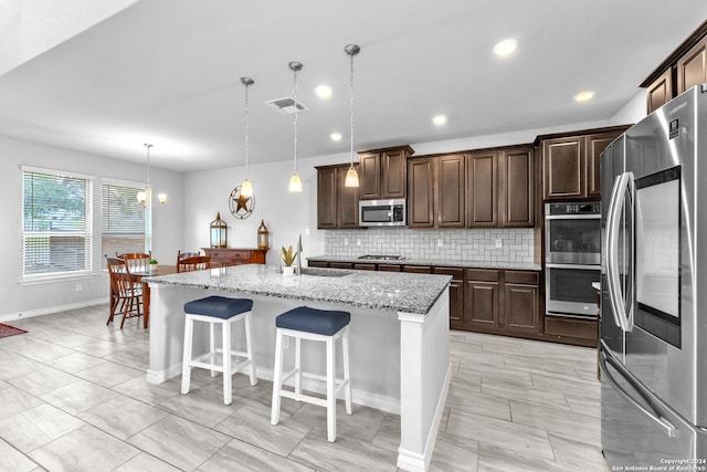 kitchen with pendant lighting, a kitchen island with sink, sink, light stone counters, and stainless steel appliances