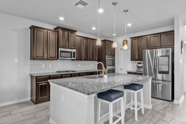 kitchen with sink, an island with sink, decorative light fixtures, dark brown cabinets, and appliances with stainless steel finishes