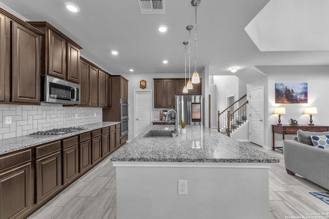 kitchen featuring sink, tasteful backsplash, an island with sink, pendant lighting, and appliances with stainless steel finishes