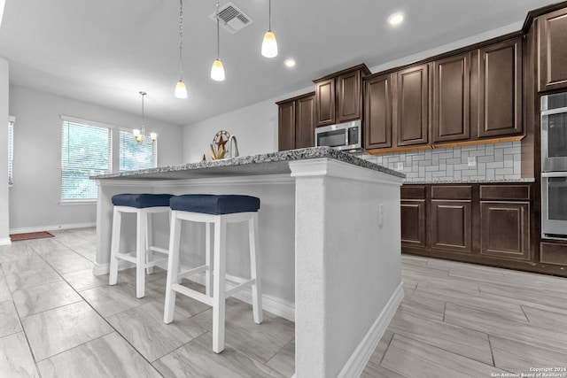 kitchen with hanging light fixtures, stainless steel appliances, backsplash, dark brown cabinets, and a kitchen island