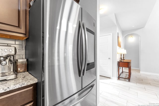 kitchen with dark brown cabinets, stainless steel fridge, and light stone counters