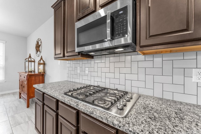 kitchen with light stone countertops, light tile patterned floors, tasteful backsplash, dark brown cabinets, and stainless steel appliances