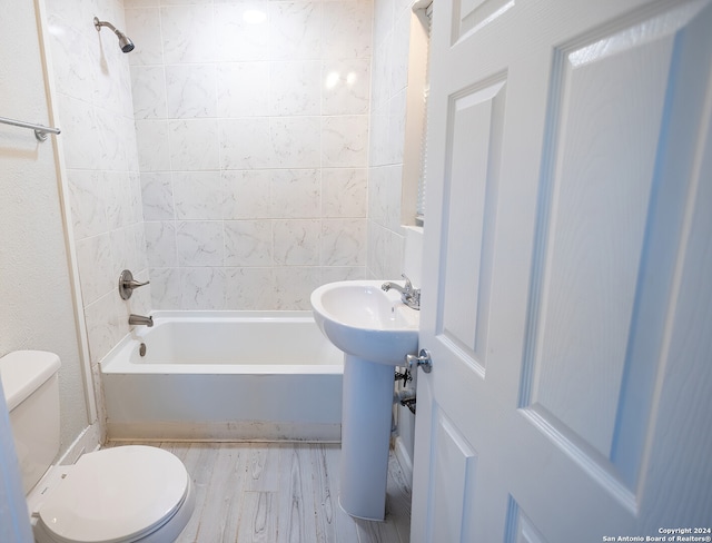 bathroom with wood-type flooring, tiled shower / bath, and toilet