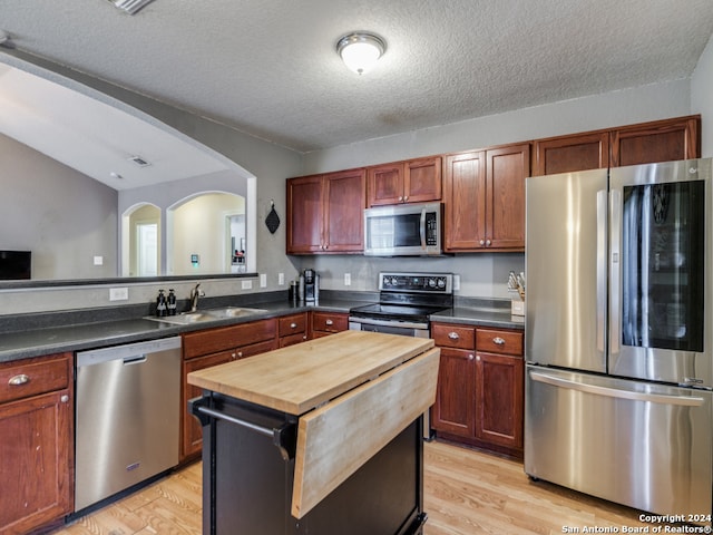 kitchen with a textured ceiling, stainless steel appliances, sink, and light hardwood / wood-style flooring