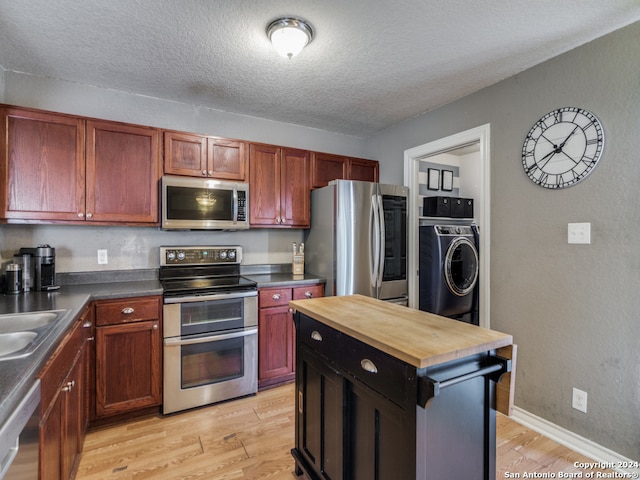 kitchen featuring light wood-type flooring, washer / clothes dryer, a textured ceiling, appliances with stainless steel finishes, and butcher block countertops