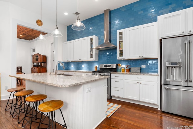 kitchen with wall chimney exhaust hood, stainless steel appliances, a center island with sink, and dark wood-type flooring