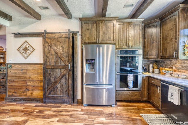 kitchen featuring light hardwood / wood-style floors, a textured ceiling, beam ceiling, a barn door, and stainless steel appliances