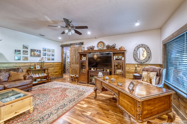 living room featuring ceiling fan, wooden walls, hardwood / wood-style floors, and a barn door