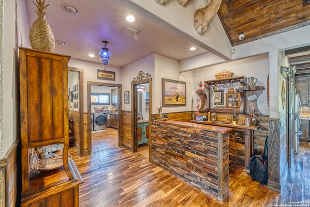 bar featuring wood-type flooring, stainless steel refrigerator, beam ceiling, and a textured ceiling