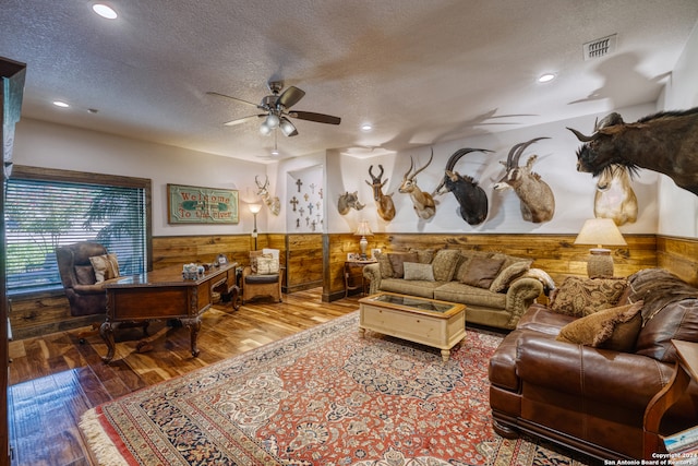 living room featuring wood-type flooring, wood walls, ceiling fan, and a textured ceiling