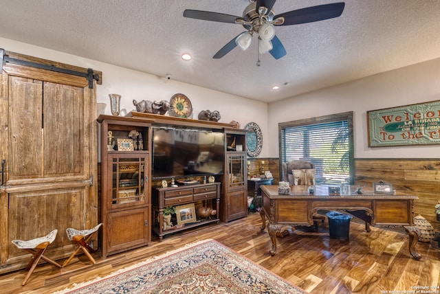 office space with ceiling fan, wood walls, a textured ceiling, light wood-type flooring, and a barn door