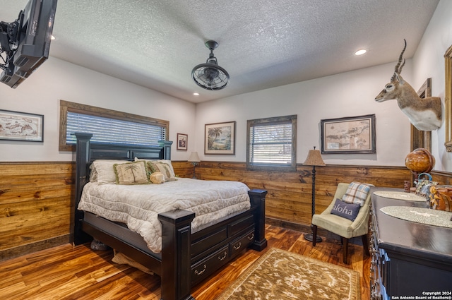 bedroom featuring wood walls, a textured ceiling, and hardwood / wood-style floors