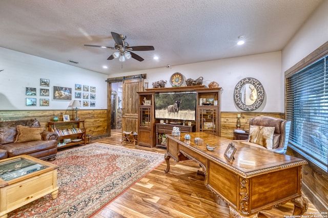 office space with ceiling fan, wood walls, a barn door, and wood-type flooring