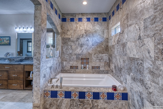 bathroom with tiled tub, vanity, and a textured ceiling