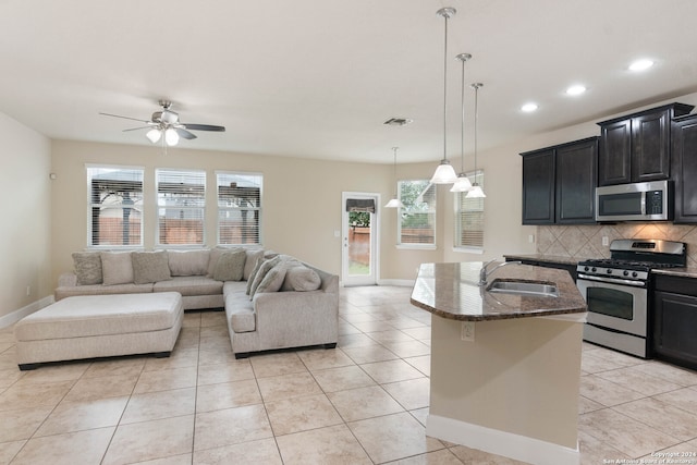 interior space featuring hanging light fixtures, an island with sink, stainless steel appliances, ceiling fan, and sink