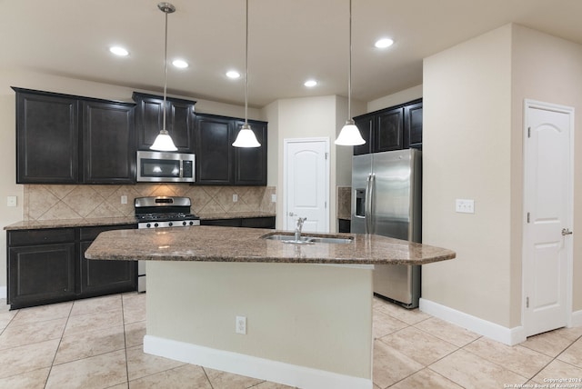 kitchen featuring sink, decorative light fixtures, a center island with sink, stainless steel appliances, and dark stone counters