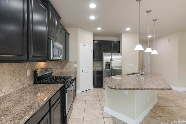 kitchen with dark stone counters, sink, an island with sink, hanging light fixtures, and appliances with stainless steel finishes