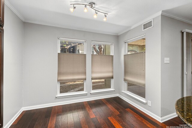 empty room with rail lighting, dark wood-type flooring, visible vents, baseboards, and ornamental molding