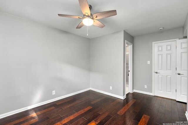 empty room featuring dark wood-type flooring, a ceiling fan, and baseboards