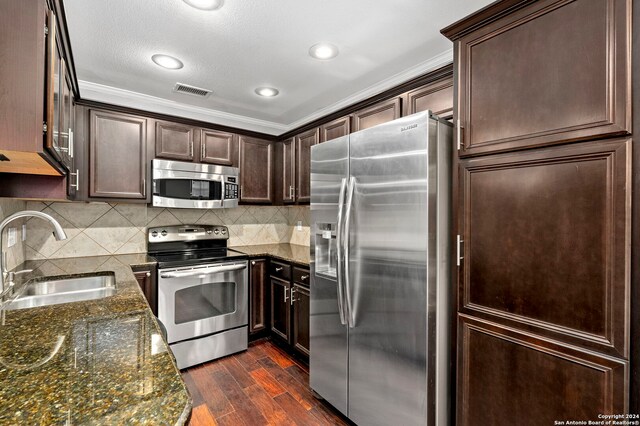 kitchen featuring a sink, stainless steel appliances, dark stone countertops, dark wood-type flooring, and dark brown cabinets