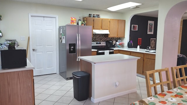 kitchen with light tile patterned floors, kitchen peninsula, backsplash, stainless steel appliances, and a center island