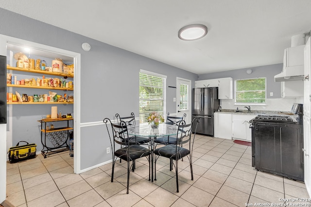 kitchen with white cabinets, light tile patterned floors, tasteful backsplash, stainless steel refrigerator, and black stove