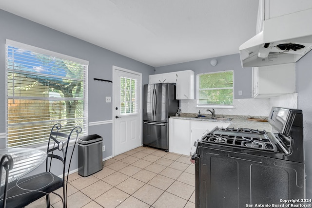 kitchen featuring stainless steel fridge, tasteful backsplash, white cabinets, light tile patterned floors, and gas range oven