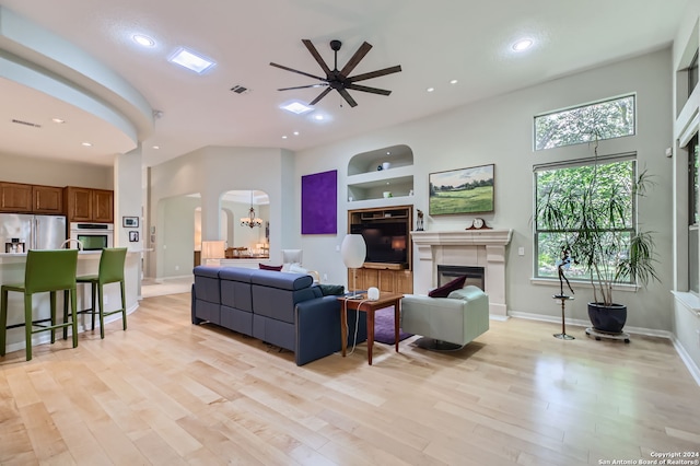 living room featuring built in shelves, ceiling fan with notable chandelier, and light wood-type flooring