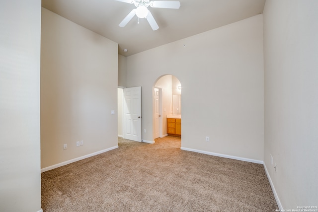 interior space with ensuite bath, ceiling fan, light colored carpet, and vaulted ceiling