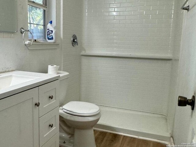 bathroom featuring wood-type flooring, tiled shower, vanity, and toilet